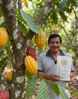 Cacao farmer holding a bag of Ceremonial Cacao Drops among cacao trees