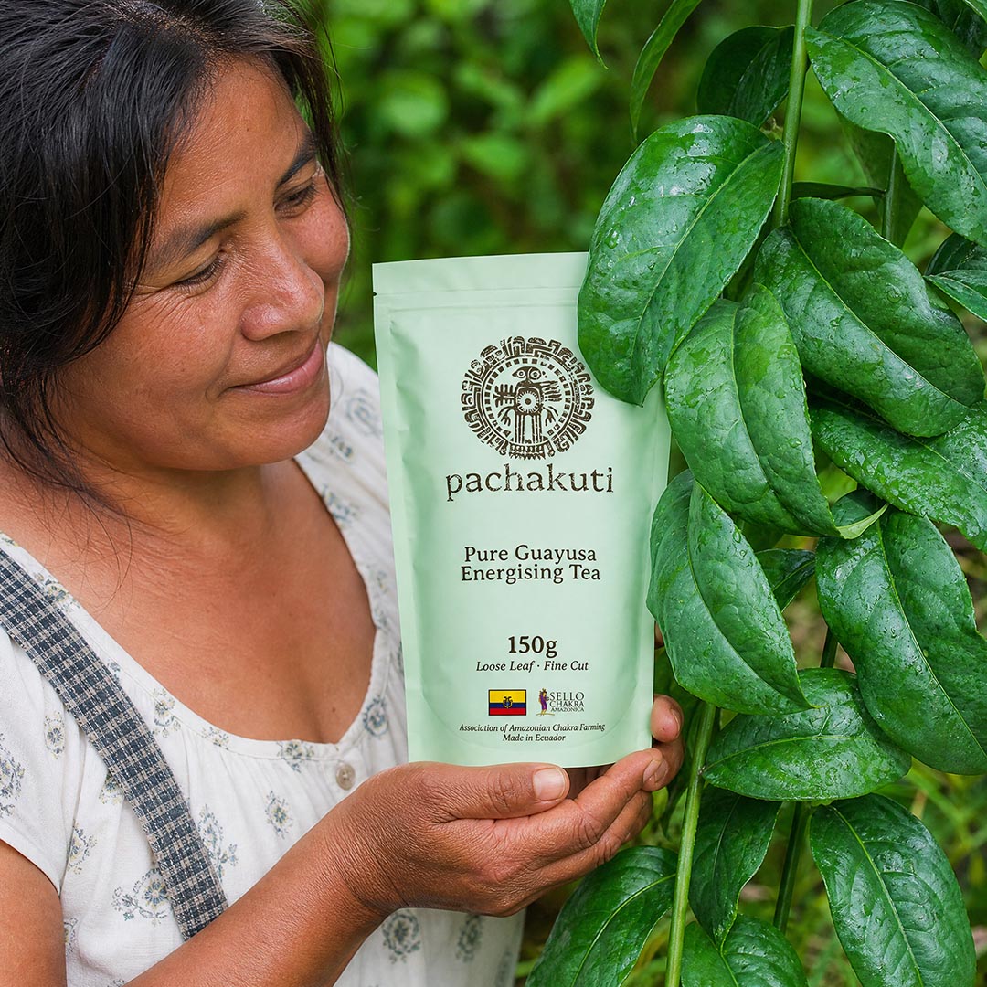 Woman holding a bag of Guayusa tea beside a guayusa plant