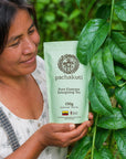 Woman holding a bag of Guayusa tea beside a guayusa plant