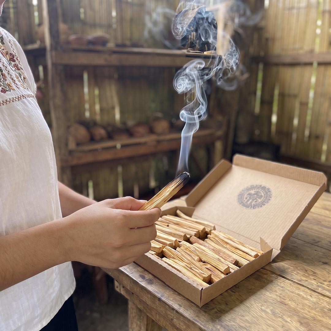 Burning Palo Santo stick held over an open box of sticks