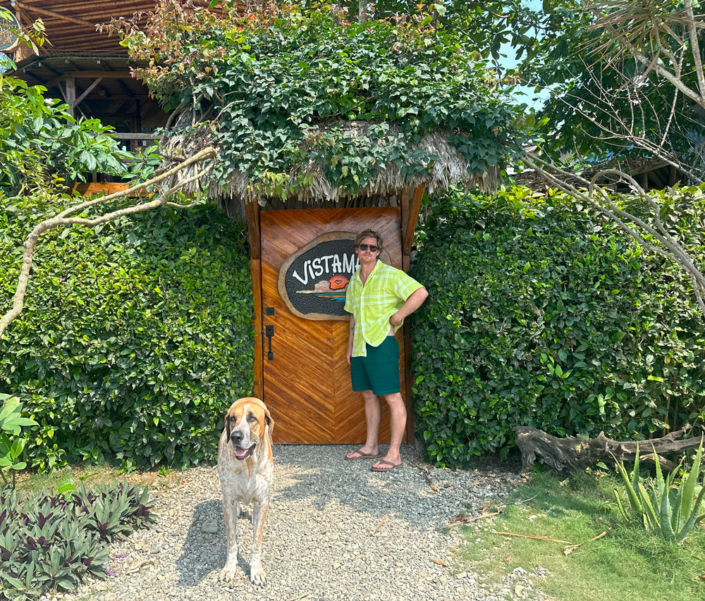 Person standing by Vistamar entrance with a friendly dog in a lush green garden setting.