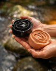 Hands holding Witoca coffee and cacao soaps by a stream